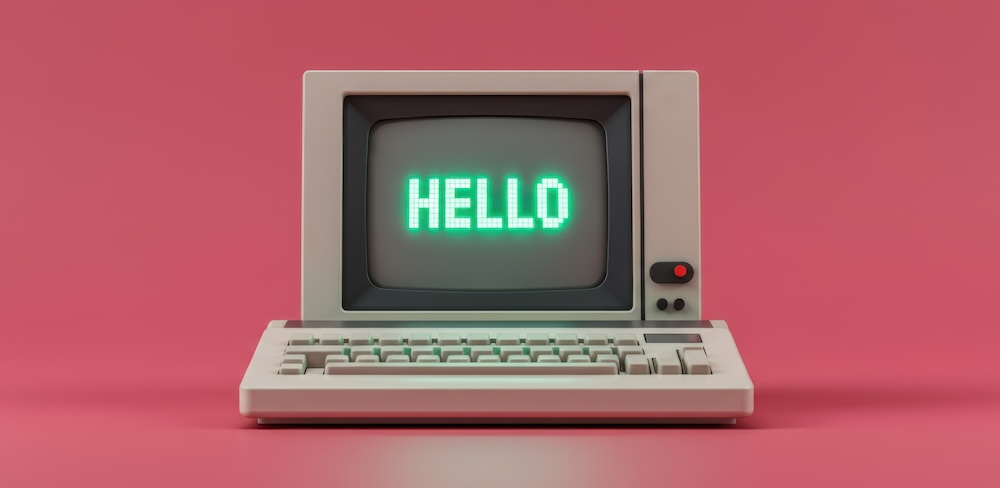 Vintage computer displays hello message against a pastel pink background