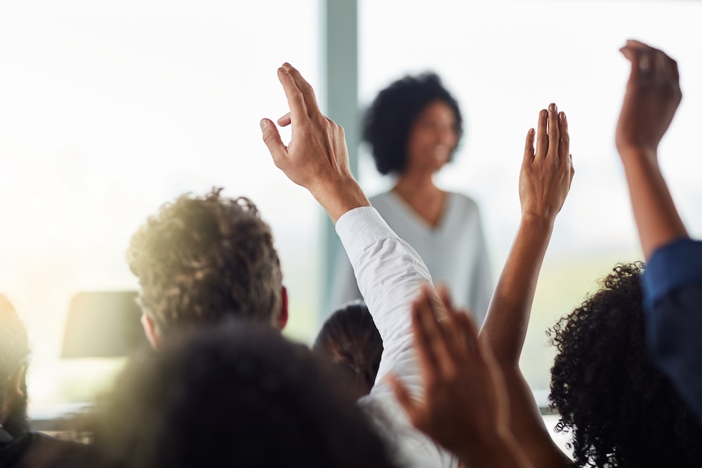 business people and hands raised for questions at conference, seminar or meeting. Group, audience and hand up for question, asking or answer, crowd vote and training at workshop presentation